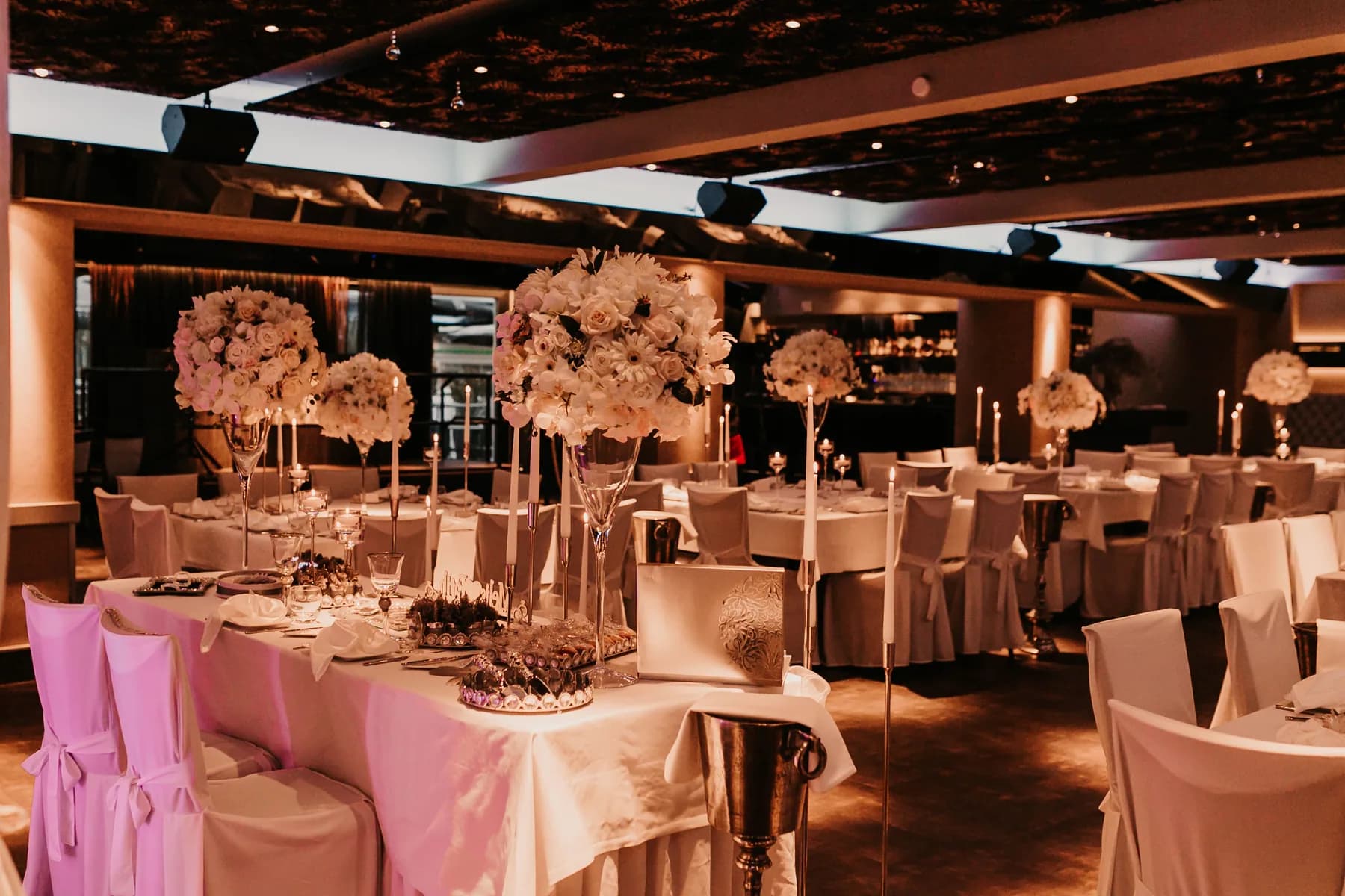 Hochzeitlich eingedeckter großer Saal im Angerhof mit weißen Hussen und hohen Blumengestecken